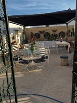 Ein Terrassenbereich im Freien mit Tisch und Stühlen, einer überdachten Sitzgelegenheit und dekorativen Wandverkleidungen.