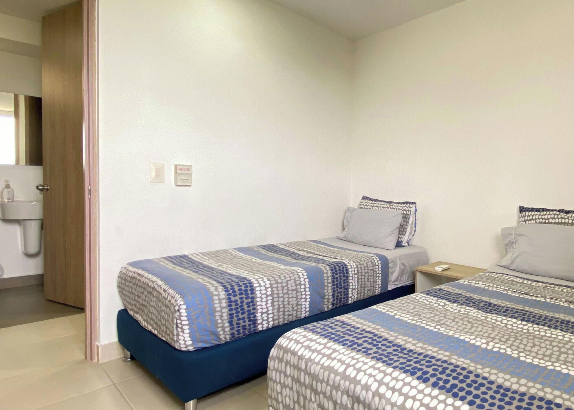 Una camera d'albergo con due letti, un comodino e un bagno visibile tramite una porta aperta.