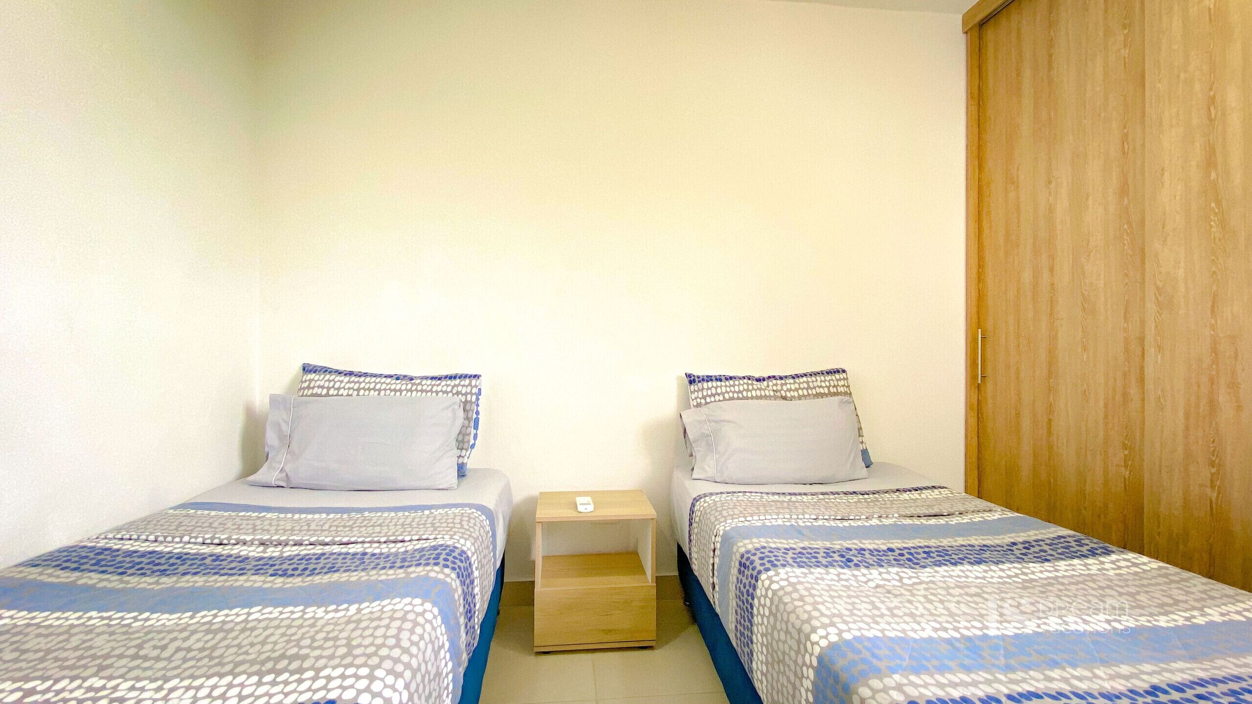Een kleine, schone kamer met twee eenpersoonsbedden, een houten garderobe en een nachtkastje met een lamp.