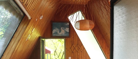 A room with a sloped ceiling, a bed, a small table, a bench, and a view through a window.
