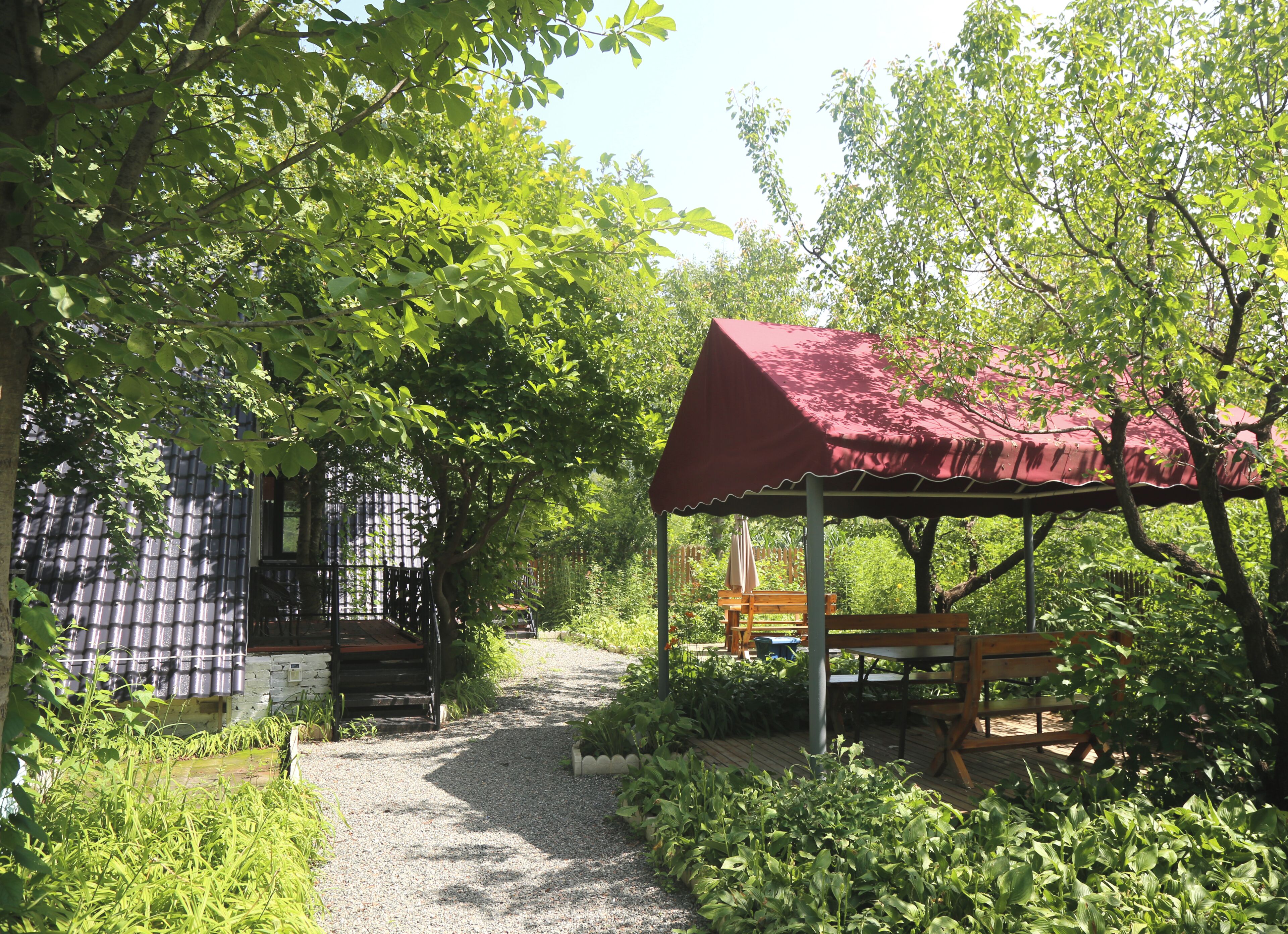 A covered outdoor seating area with a gravel path leading to a building with a metal fence.