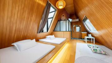 Een gezellig, driehoekig vertrek met houten wanden, twee bedden, een kleine tafel en een raam.