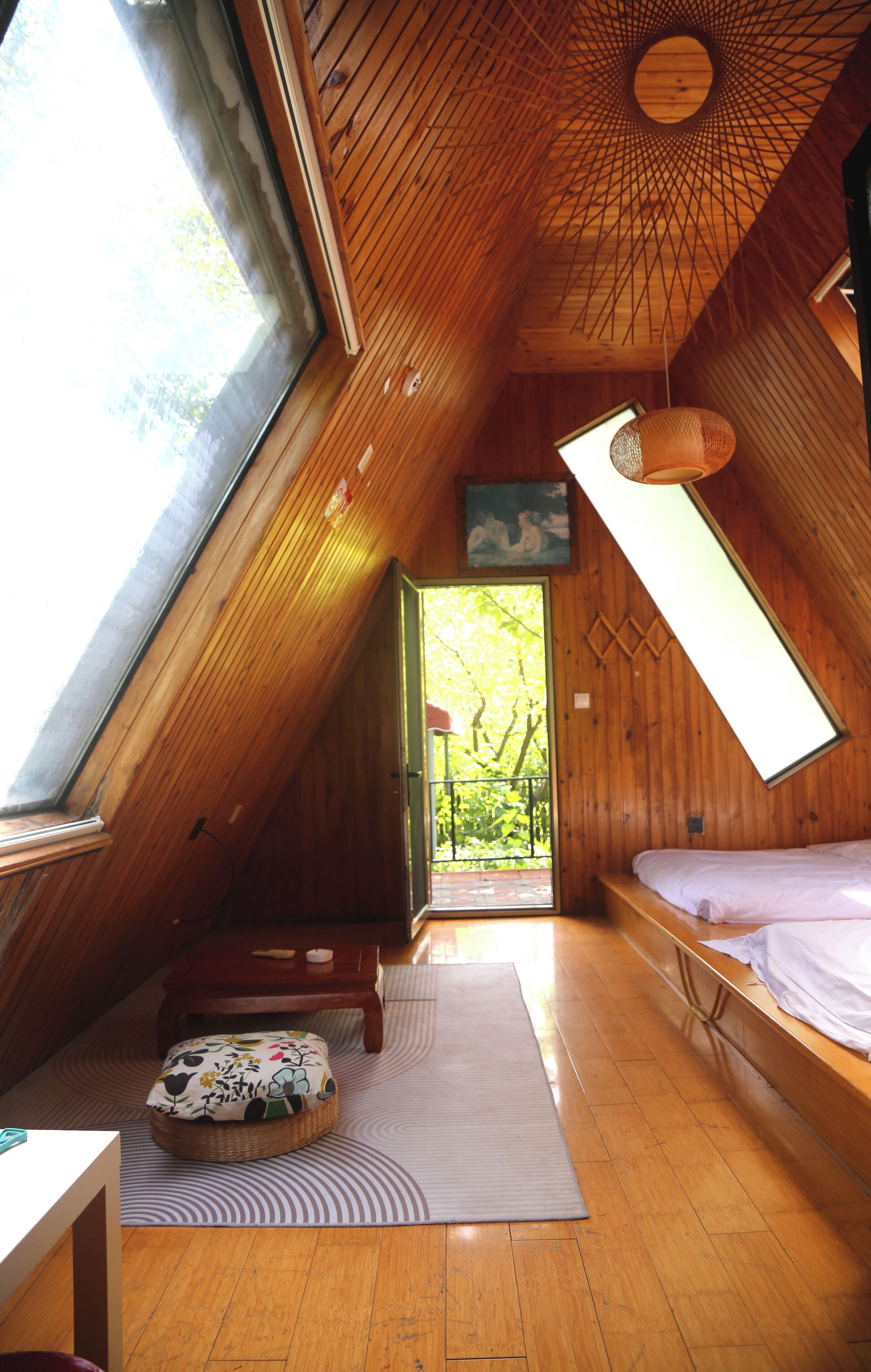 A room with a sloped ceiling, a bed, a window, and a door leading outside.