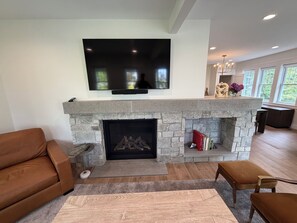 A living room with a stone fireplace, a flat-screen TV mounted above it, and a sofa. - Steps to Beach! Newly Renovated 4BR Lakeview w Wrap Porch Game Garage Fire Pit (South Haven)