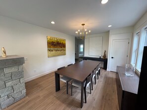 A modern kitchen with a dining area, stone fireplace, and artwork on the wall. - Steps to Beach! Newly Renovated 4BR Lakeview w Wrap Porch Game Garage Fire Pit (South Haven)