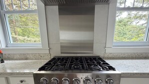 Una cucina con un piano cottura Viking in acciaio inossidabile, mobili bianchi e una finestra che si affaccia su degli alberi.