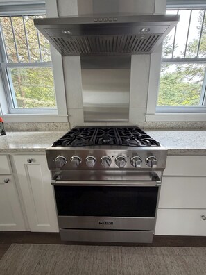 A kitchen with a stainless steel Viking stove, white cabinetry, and a window with a view of trees. - Steps to Beach! Newly Renovated 4BR Lakeview w Wrap Porch Game Garage Fire Pit (South Haven)