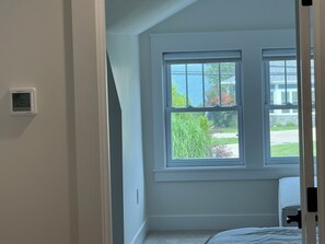 A bedroom with a large window, a thermostat, and a bed. - Steps to Beach! Newly Renovated 4BR Lakeview w Wrap Porch Game Garage Fire Pit (South Haven)