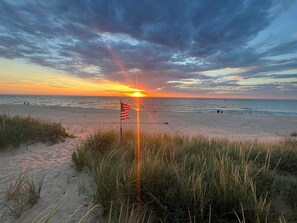 A beach with an American flag, waves, and a sunset. - Steps to Beach! Newly Renovated 4BR Lakeview w Wrap Porch Game Garage Fire Pit (South Haven)
