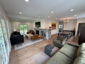 A spacious living area with a fireplace, seating, and a dining area. - Steps to Beach! Newly Renovated 4BR Lakeview w Wrap Porch Game Garage Fire Pit (South Haven)