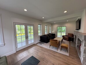 A spacious living room with a fireplace, large windows, and a balcony. - Steps to Beach! Newly Renovated 4BR Lakeview w Wrap Porch Game Garage Fire Pit (South Haven)