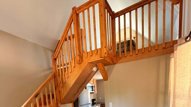 Ein Loft-Zimmer mit einer Holztreppe, einem Essbereich mit rundem Tisch und Stühlen, und einer Küche im Hintergrund.