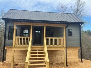 A two-story building with a front porch, a staircase leading to the entrance, and a metal roof. - Cozy Pine 1-bedroom cabin in gorgeous Old Fort with AC (Old Fort)