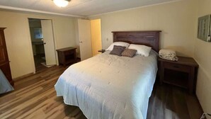 Een slaapkamer met een bed, nachtkastjes, een nachttafeltje, een houten hoofdbord en een deur naar een andere kamer.