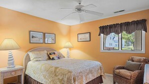 A bedroom with a bed, two bedside lamps, a chair, a ceiling fan, and framed pictures on the wall. - Eagle Way 2 - Access to Pools (Rehoboth Beach)