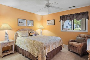 Ein Schlafzimmer mit einem Bett, zwei Nachttischlampen, einem Sessel, einem Deckenventilator und gerahmten Bildern an der Wand.
