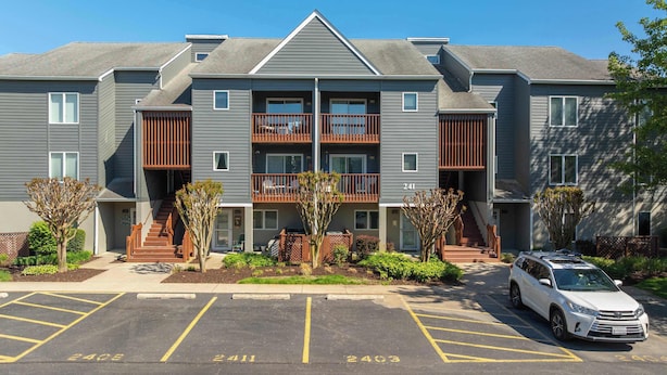 A multi-story residential building with balconies, a parking lot, and a white SUV parked in front. - Eagle Way 2 - Access to Pools (Rehoboth Beach)