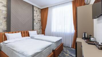 Une chambre d’hôtel avec deux lits, un bureau, une télévision et une fenêtre avec des rideaux.