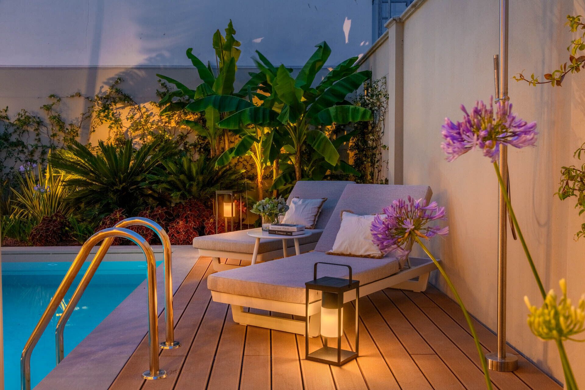 A poolside lounge area with a cushioned seating arrangement, a small table, and a lantern.