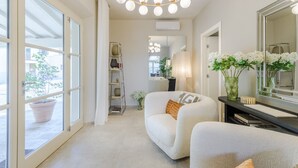 A modern hotel room with a large mirror, a sofa, a chair, a potted plant, and a view through the window. - The Secret Garden Cottage (Lucca)