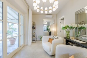 Ein modernes Hotelzimmer mit einem großen Spiegel, einer Couch, einem Sessel, einer Topfpflanze und Blick aus dem Fenster.