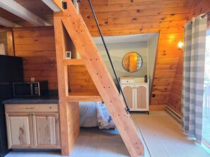Un intérieur en bois avec un lit en mezzanine, un four à micro-ondes et un placard.