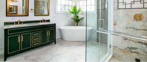 A bathroom with a freestanding bathtub, a glass shower enclosure, and a dark green vanity with gold handles.