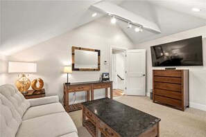 A modern living room with a sloped ceiling, a flat-screen TV, a wooden cabinet, a sofa, and a coffee table. - Tiny Homes | Low Country with Studio (Richmond)