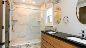 Une salle de bain avec une douche, un lavabo, un miroir et un meuble-lavabo en bois.