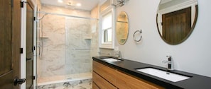 A bathroom with a shower, a sink, a mirror, and a wooden vanity.