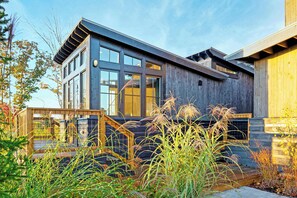 Une maison moderne à deux étages, dotée de grandes fenêtres, d’un revêtement extérieur en bois et d’une terrasse en bois.
