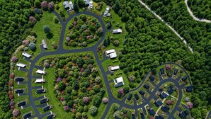 Une vue aérienne d’un quartier résidentiel où les maisons sont disposées en cercle, entourées de pelouses verdoyantes et d’arbres.
