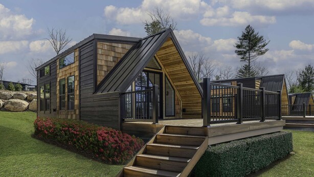 A modern cabin with a sloped roof, large windows, and a wooden deck.