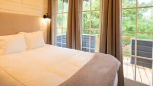 A bedroom with a large bed, two wall-mounted lights, and a view of the outdoors through a window.