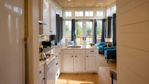 A modern kitchen with white cabinets, a central island, and a blue sofa in a bright room with large windows.