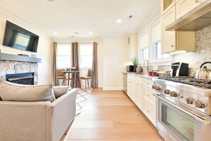 A modern kitchen with a flat-screen TV, a stone fireplace, a dining area with a table and chairs, and a sofa. - Hilltop | Standard Queen (Richmond)