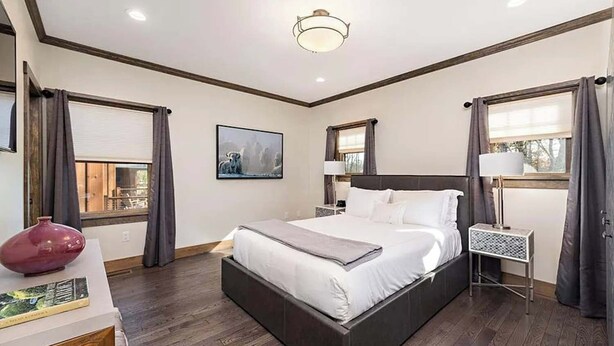 Une chambre à coucher avec un grand lit, une table de chevet, une lampe, un tableau au mur et une fenêtre avec des rideaux.