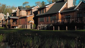 Un grand chalet à plusieurs étages, doté d’un porche imposant et d’un étang en premier plan.