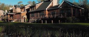 A large, multi-story lodge with a prominent porch and a pond in the foreground.