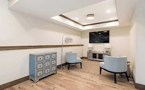 A hotel room with a wooden floor, a blue cabinet, two chairs, a TV, and a ceiling light.