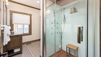 Un baño moderno con cabina de ducha de vidrio, un banco de madera y un tocador con espejo y toallero.