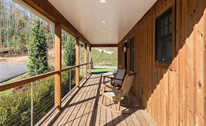 A wooden deck with a railing, a rocking chair, and a view of a road and trees. - Laurel Ridge | Three Bedroom Grand (Richmond)