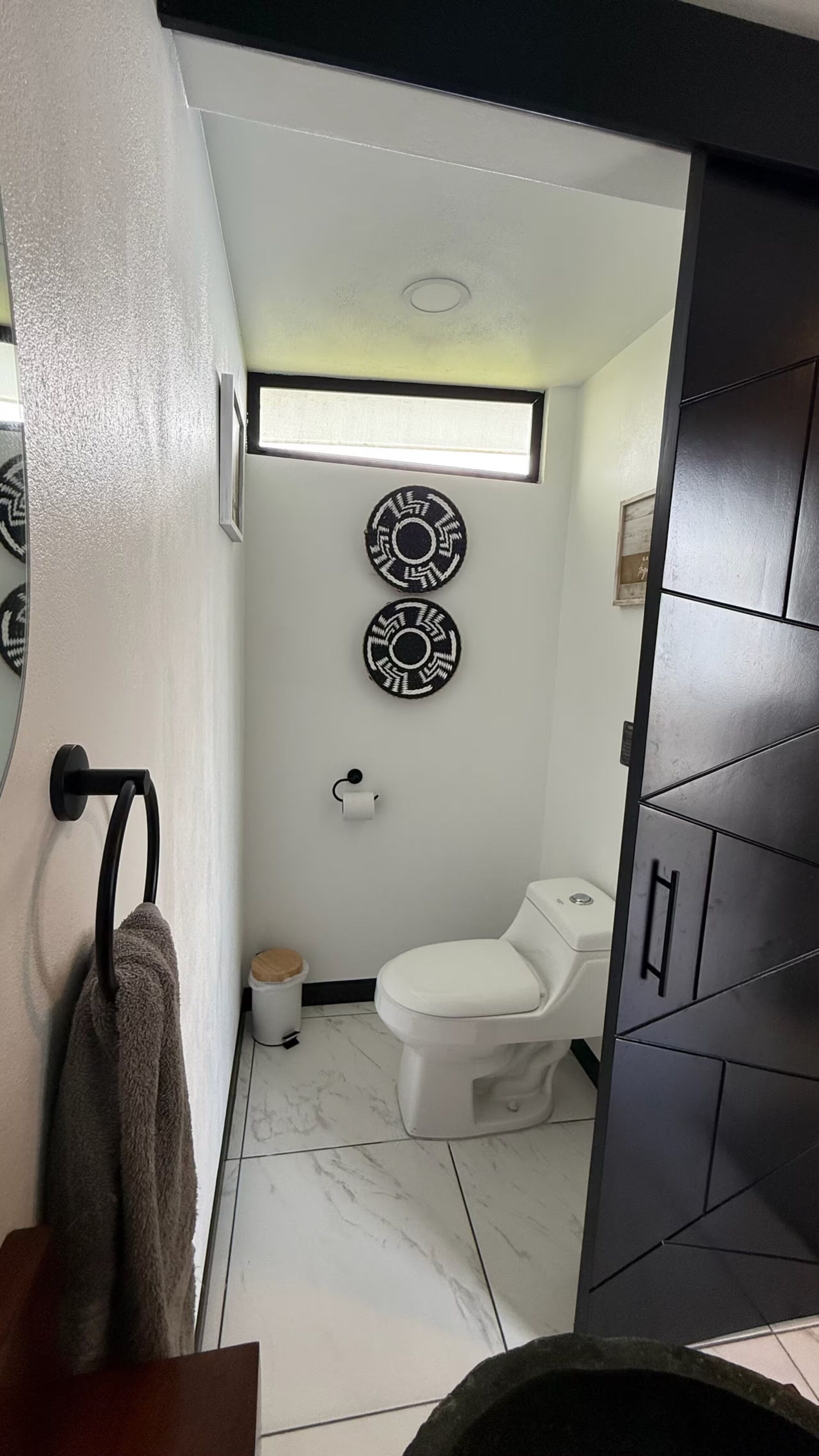 Un baño con inodoro, toallero, cubo de basura y detalles decorativos en la pared.