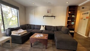 Ein Wohnzimmer mit Ecksofa, Couchtisch und Bücherregal.