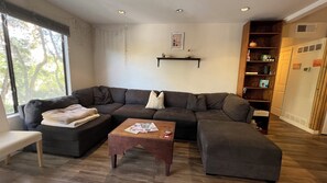Ein Wohnzimmer mit Ecksofa, Couchtisch und Bücherregal.