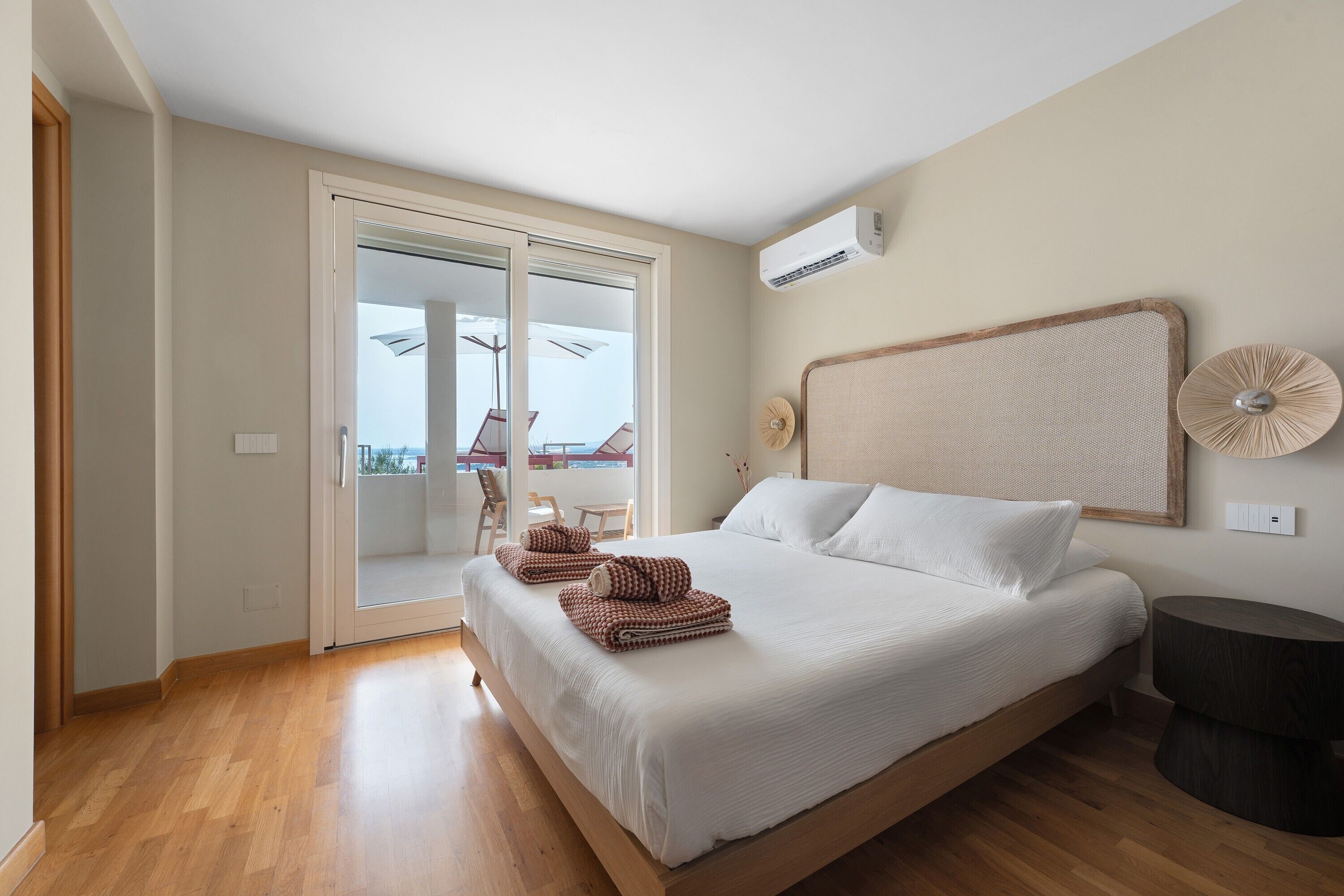 A bedroom with a bed, a sliding glass door leading to an outdoor area, a ceiling fan, and a wall-mounted air conditioning unit.