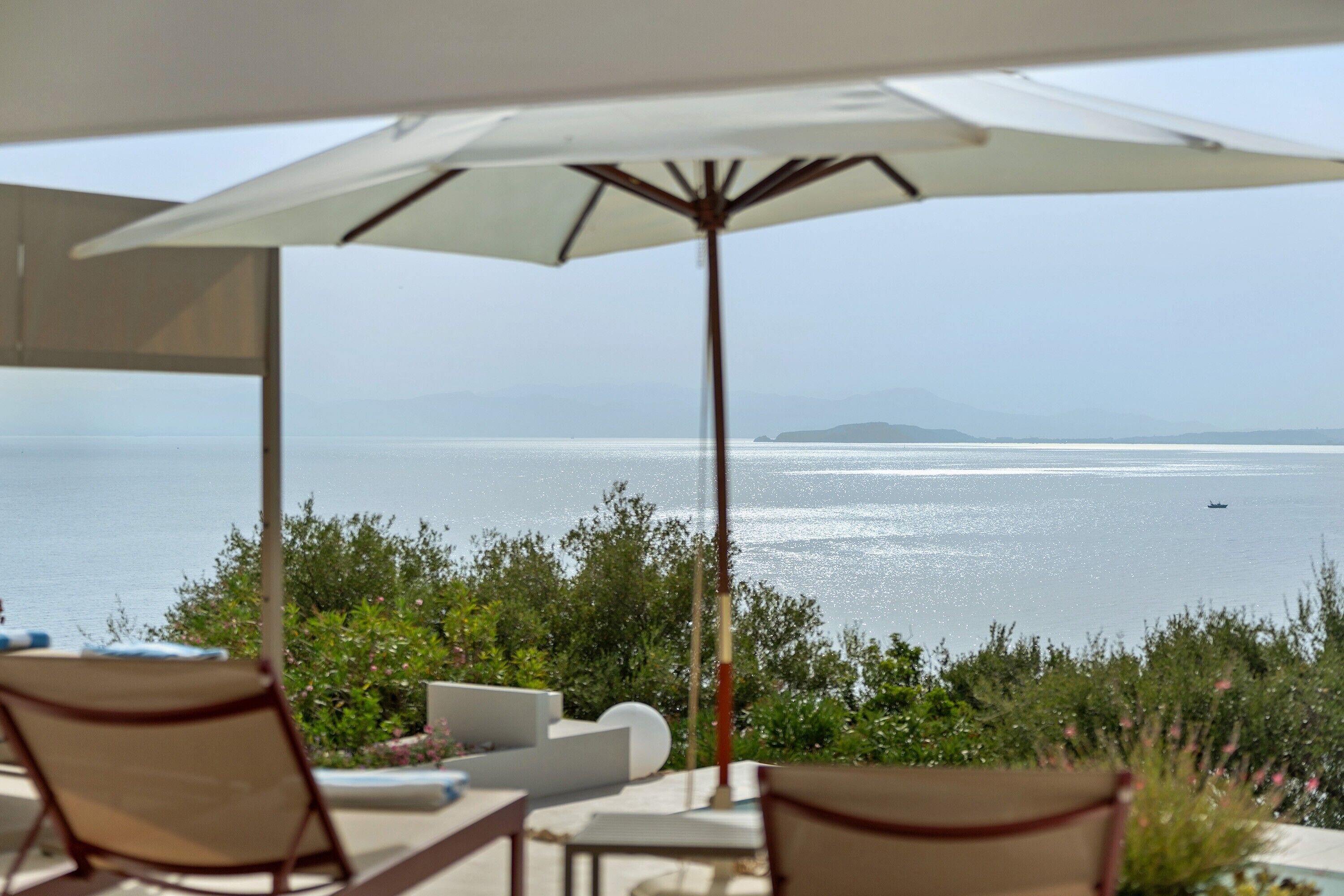 An outdoor seating area with a view of the sea and a boat in the distance.