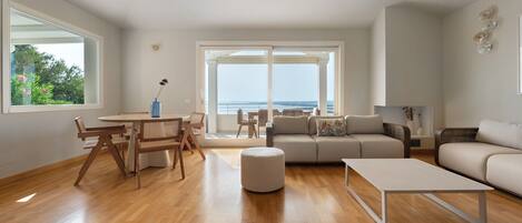 Una sala de estar moderna con suelo de madera, un sofá, una mesa de centro y un comedor con sillas y una mesa.