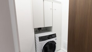 A compact laundry room with a front-loading washing machine, a drying rack, and a cabinet above.