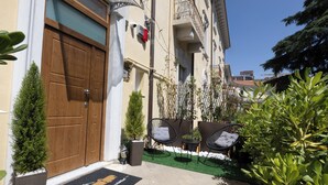 A building with a wooden door, a balcony with a railing, and a small outdoor seating area with chairs and a table.